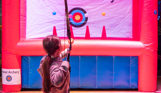 A young girl aiming a hover archery bow at the inflatable target