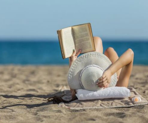 A woman laid on the beach reading a book