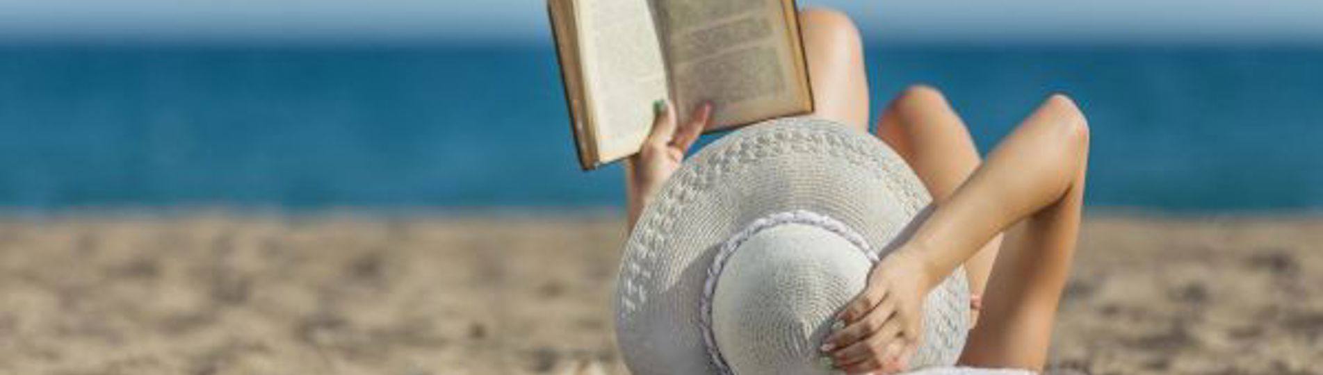 A woman laid on the beach reading a book