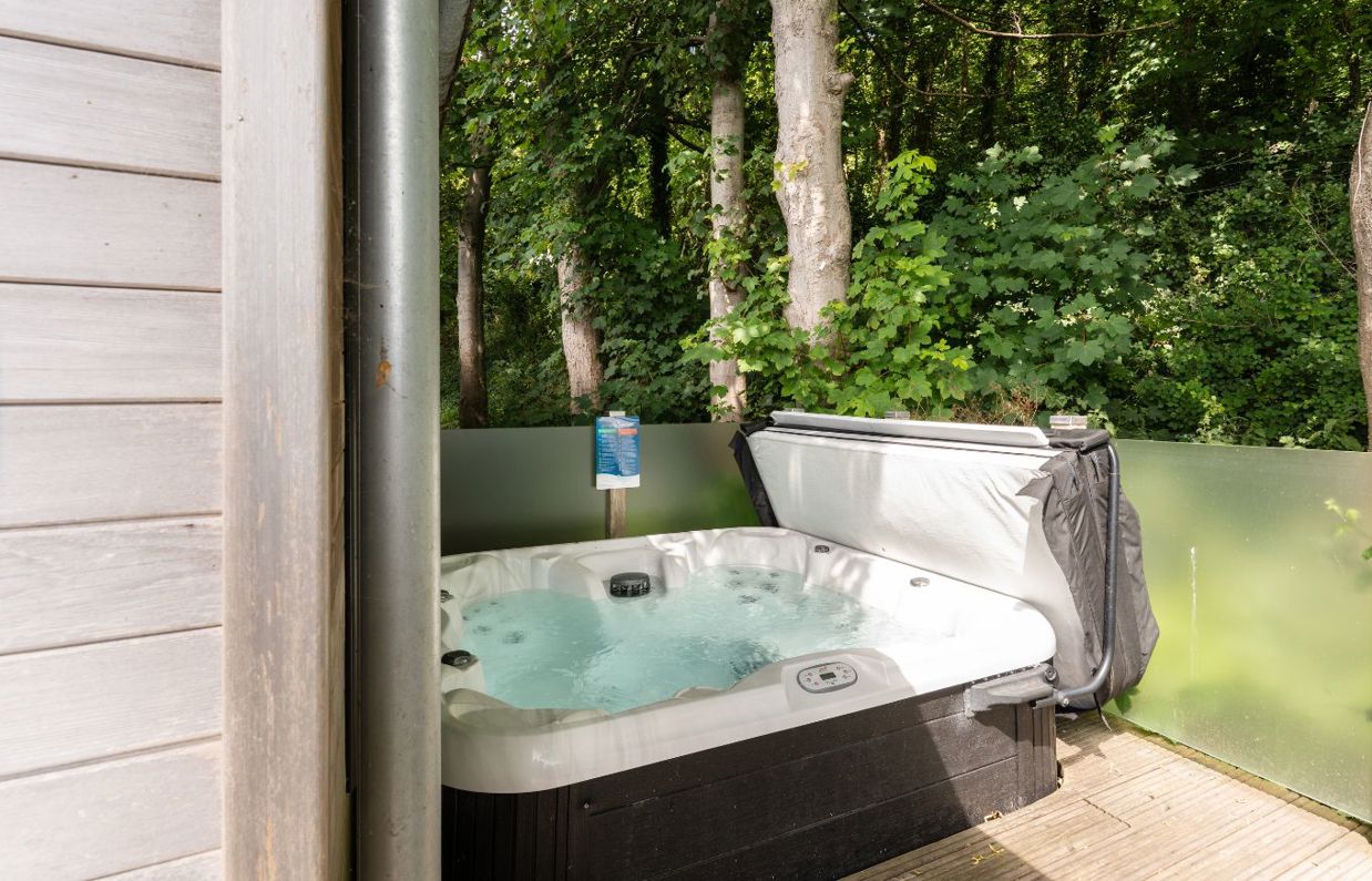 External of a lodge on pitch with hot tub among woodland