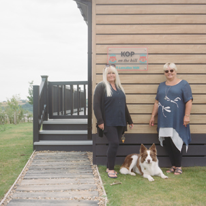Two women stood by a holiday lodge with a dog
