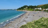 A small shingle beach at the bottom of rolling countryside hills on a sunny, blue sky day