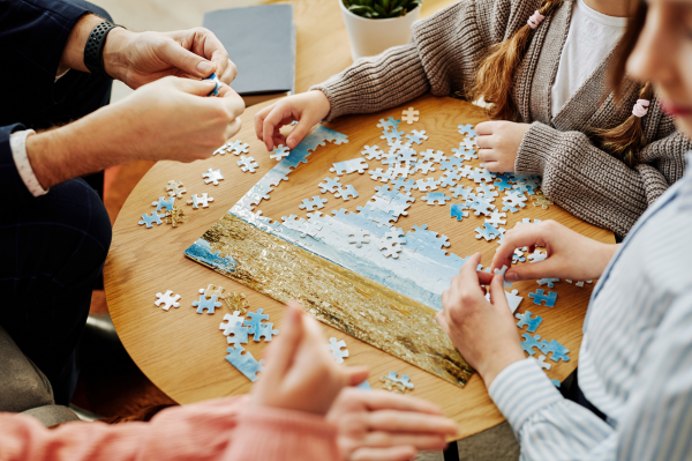 A group of people sat around a table doing a jigsaw puzzle of a beach scene
