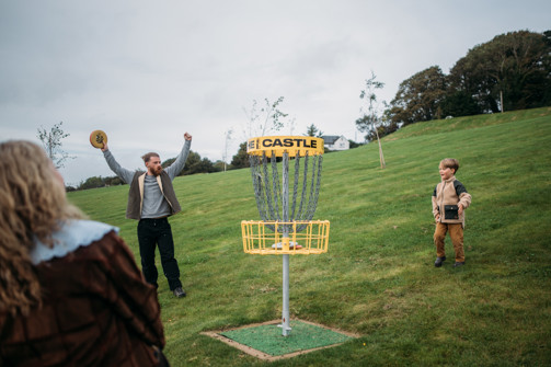 A couple with a young boy playing disc golf in a field