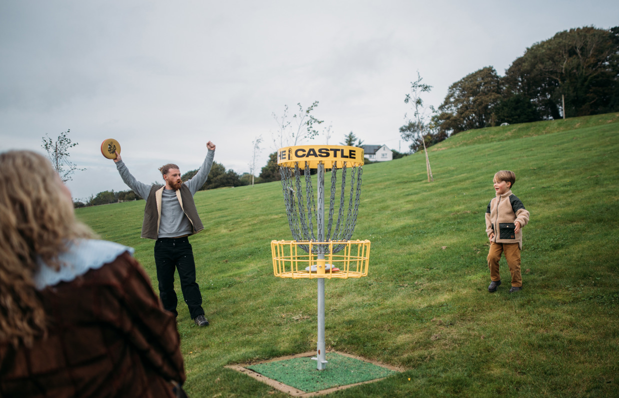 A couple with a young boy playing disc golf in a field