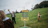 A couple with a young boy playing disc golf in a field
