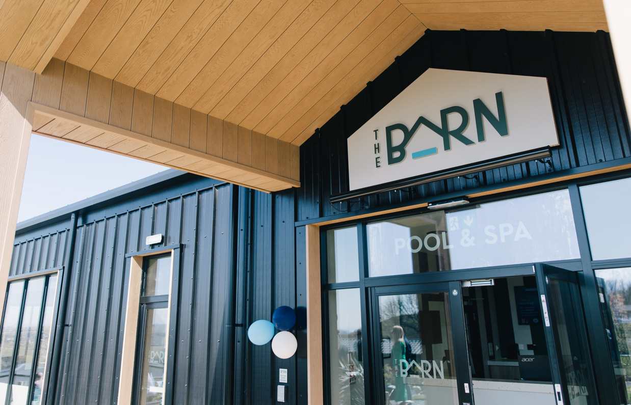 The entrance to an indoor heated swimming pool within a barn style building with boho-chic styling and countryside views