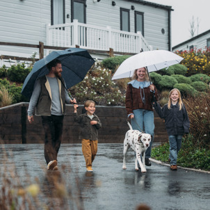 A Family of Four and a Dalmatian Cheerfully Walking Through A Caravan Park in the Rain with Umbrellas