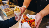 Two people's hands passing a gyros and selection of chicken legs