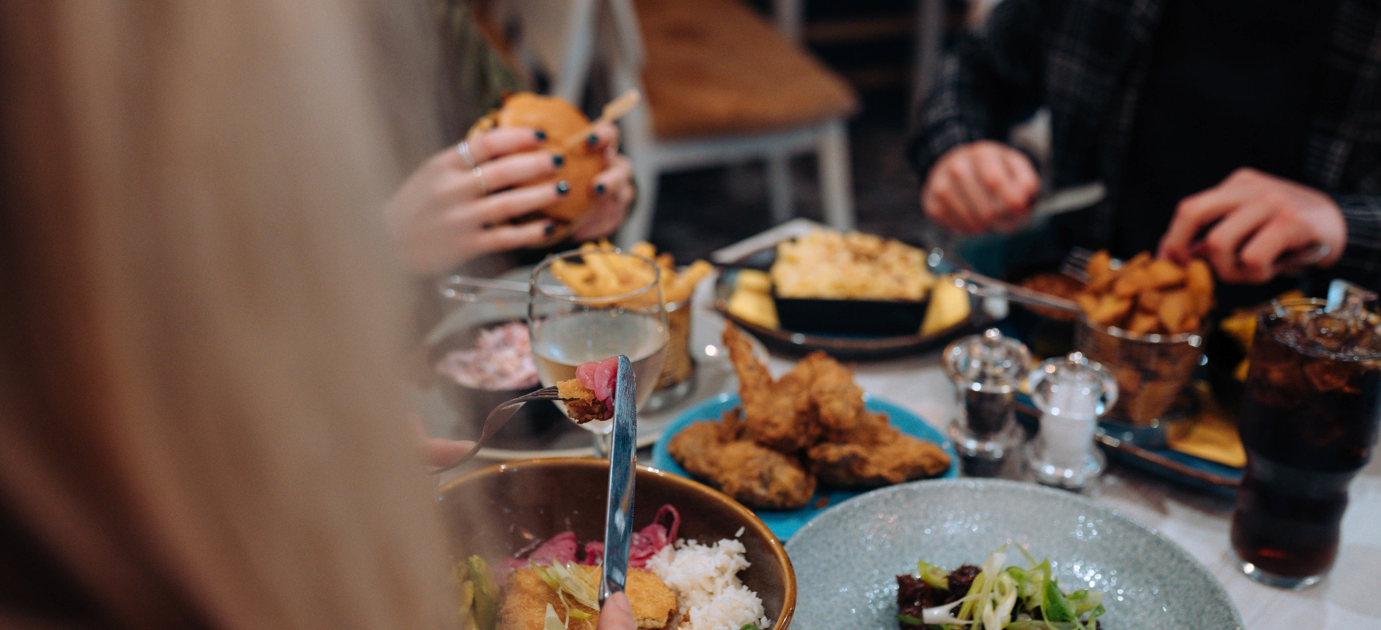 A selection of chicken, pasta, veggie and potato dishes at a table with three people eating