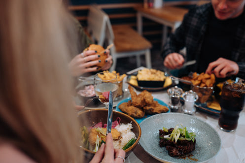 A selection of chicken, pasta, veggie and potato dishes at a table with three people eating
