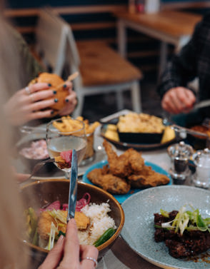 A selection of chicken, pasta, veggie and potato dishes at a table with three people eating