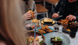 A selection of chicken, pasta, veggie and potato dishes at a table with three people eating