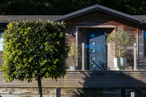 A holiday lodge with decking, plants and trees, surrounded by woodland