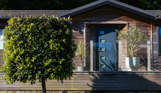 A holiday lodge with decking, plants and trees, surrounded by woodland