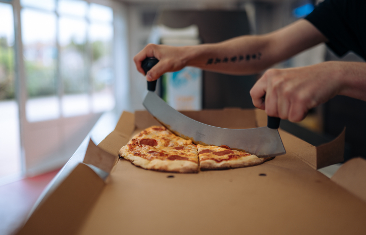 A takeaway pizza being cut in its box in a takeaway shop