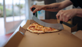 A takeaway pizza being cut in its box in a takeaway shop