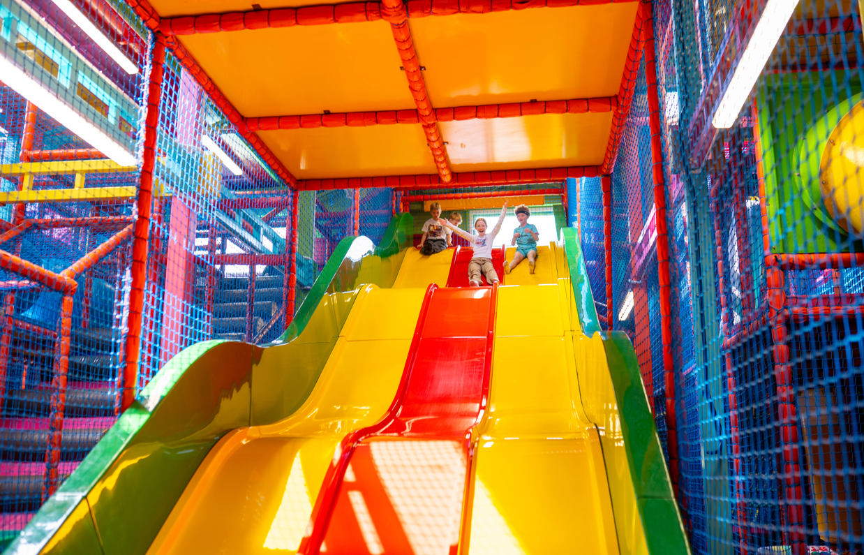 A group of young children going down a slide at a soft play