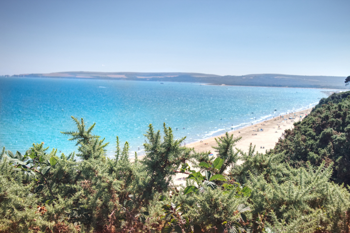 A sandy beach from high up with blue sea and hills in the background
