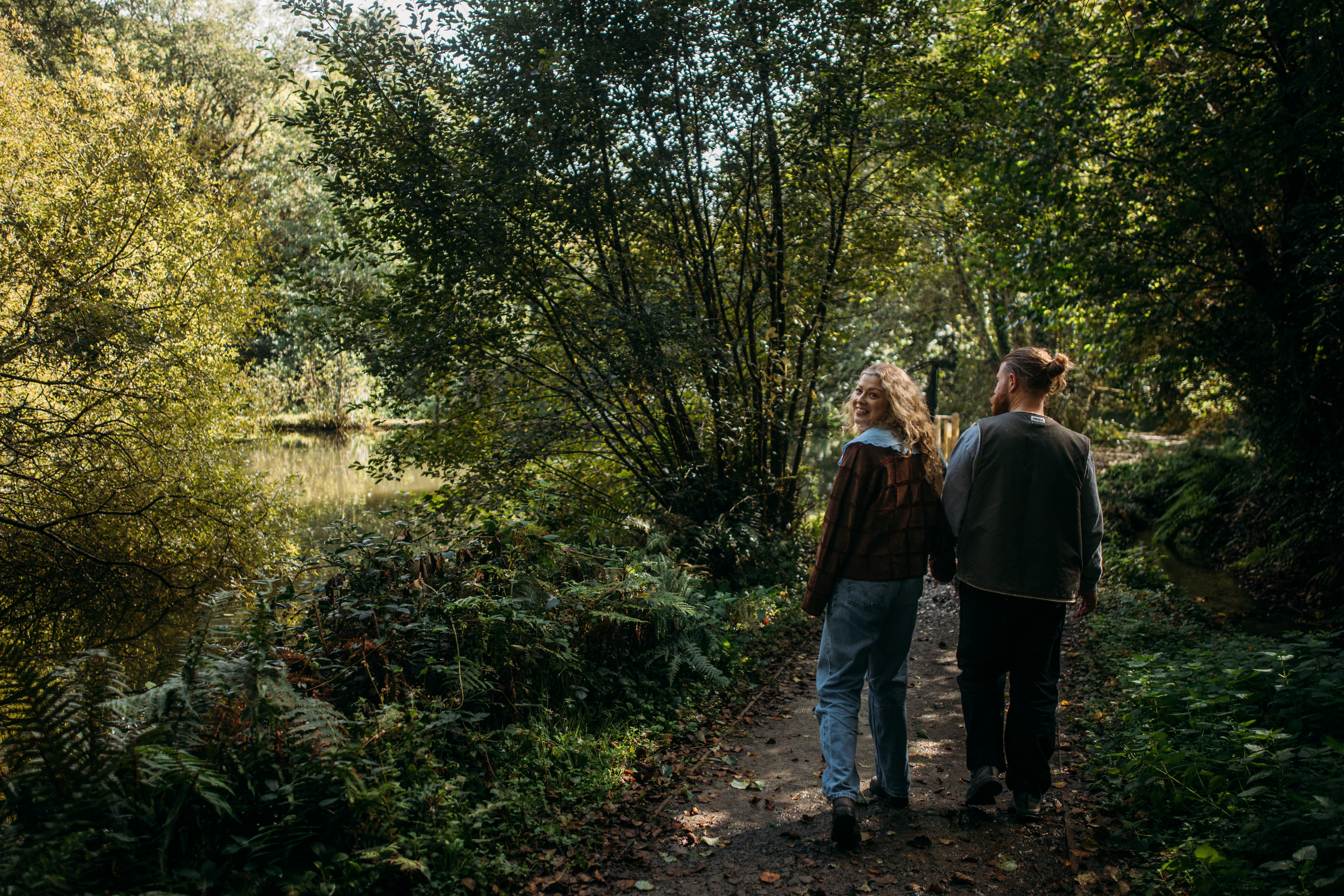 A couple walking through woodland together holding hands as the woman looks back towards the camera
