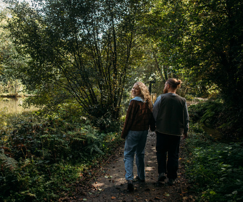 A couple walking through woodland together holding hands as the woman looks back towards the camera