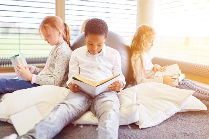 A group of young children sat back to back against an exercise ball reading books in a corner