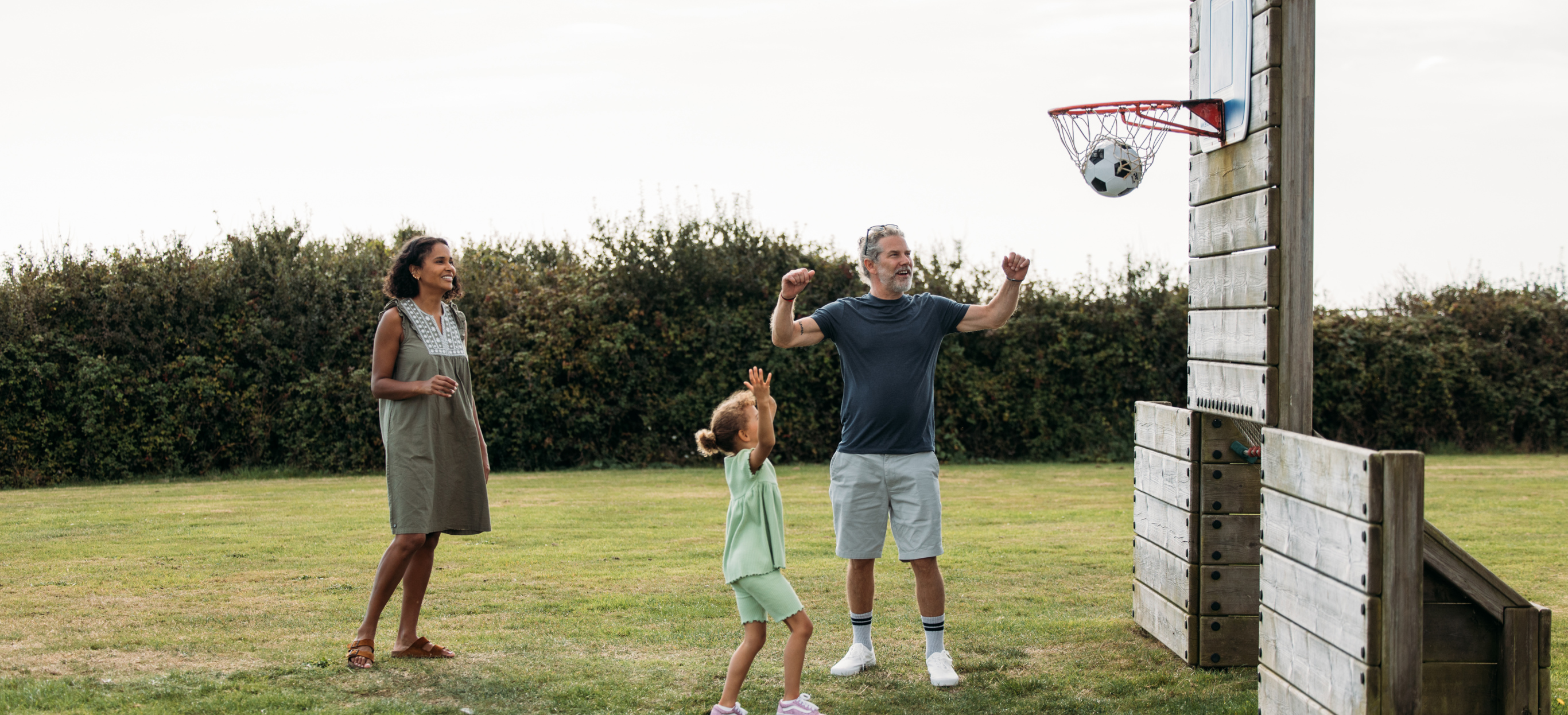 A family of three with a young girl playing basketball in a field