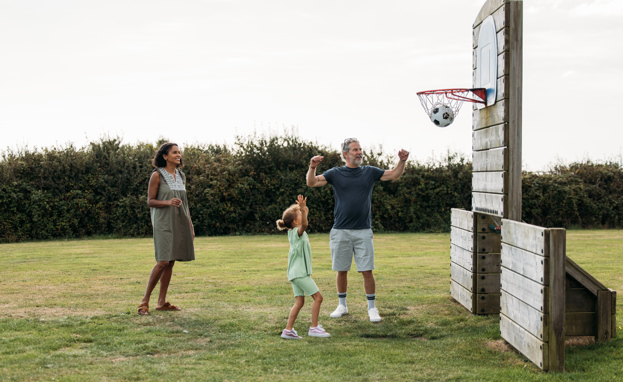 A family of three with a young girl playing basketball in a field