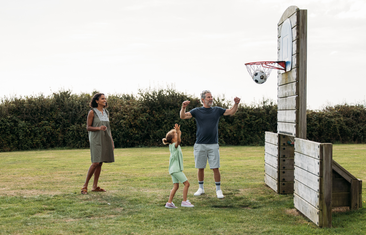 A family of three with a young girl playing basketball in a field