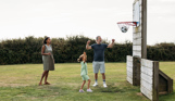 A family of three with a young girl playing basketball in a field
