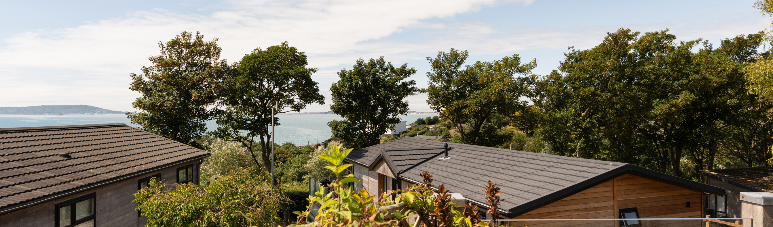 The view of the sea and Weymouth from the Kingfisher area of Osmington Mills Lodge Park surrounded by lodges and trees on a sunny, blue sky day