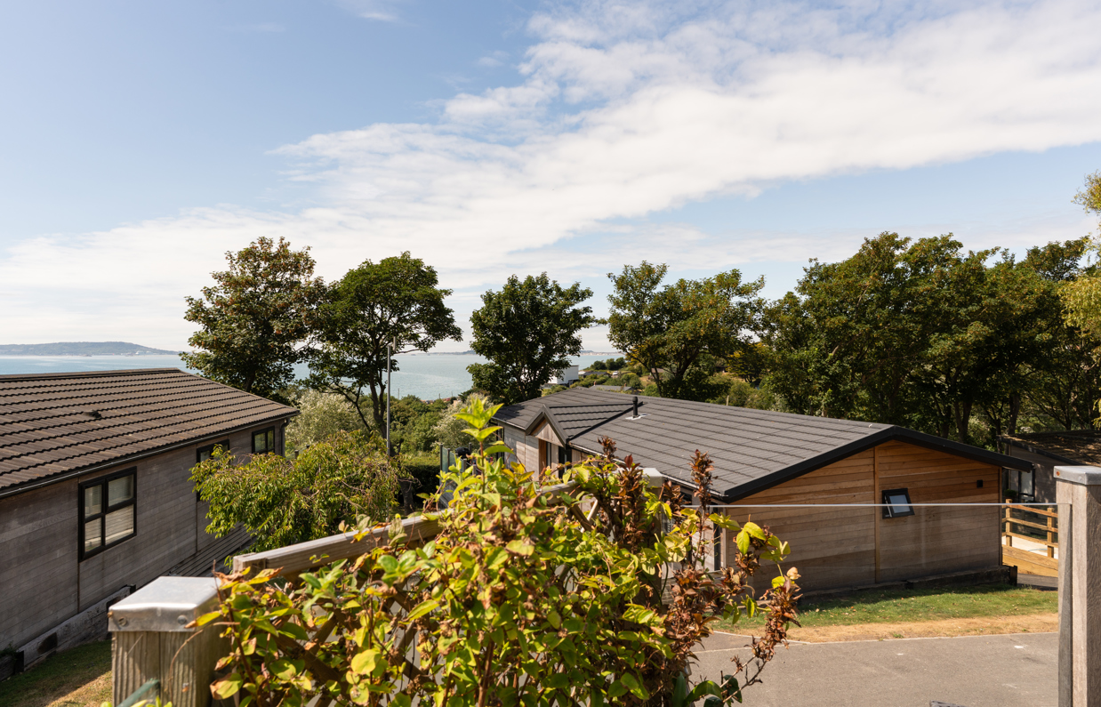 The view of the sea and Weymouth from the Kingfisher area of Osmington Mills Lodge Park surrounded by lodges and trees on a sunny, blue sky day