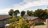 The view of the sea and Weymouth from the Kingfisher area of Osmington Mills Lodge Park surrounded by lodges and trees on a sunny, blue sky day
