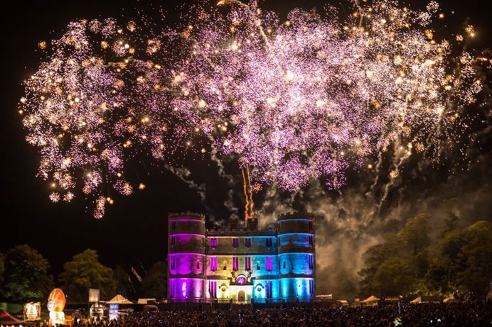 A castle lit up at night time with fireworks overhead