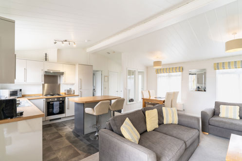 View of inside of a lodge holiday home with open plan kitchen, breakfast bar and comfy sofas
