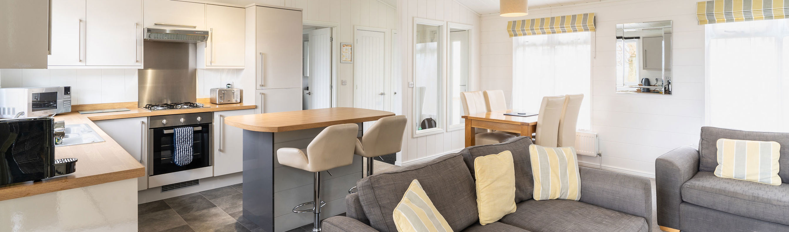 View of inside of a lodge holiday home with open plan kitchen, breakfast bar and comfy sofas