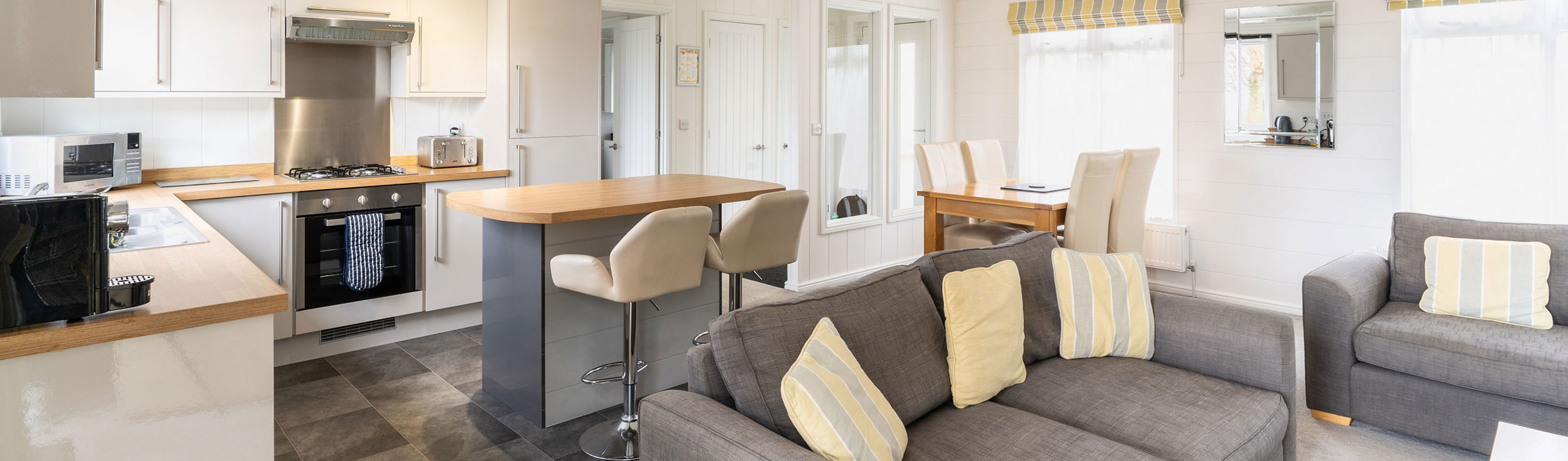 View of inside of a lodge holiday home with open plan kitchen, breakfast bar and comfy sofas