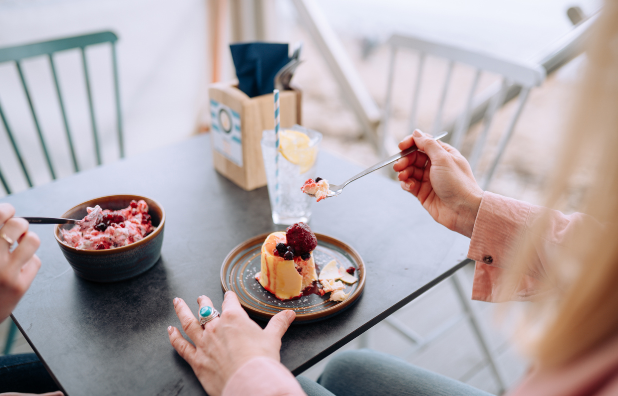 Two women sat at a table in the outside seating area of a restaurant with desserts