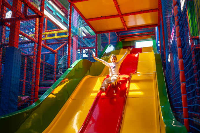 A young girl going down a large bright slide in a softplay