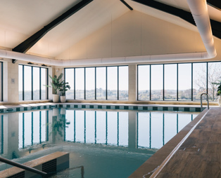 An indoor heated swimming pool within a barn style building with boho-chic styling and countryside views