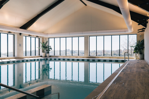 An indoor heated swimming pool within a barn style building with boho-chic styling and countryside views