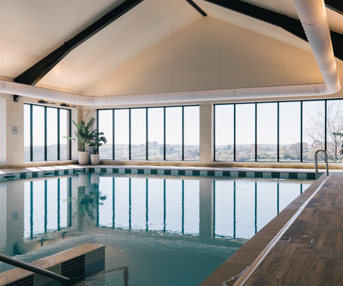 An indoor heated swimming pool within a barn style building with boho-chic styling and countryside views