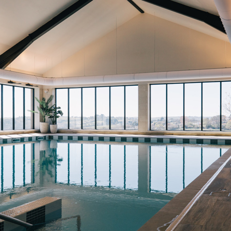 An indoor heated swimming pool within a barn style building with boho-chic styling and countryside views