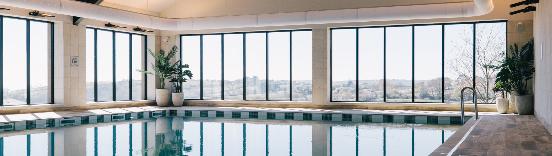 An indoor heated swimming pool within a barn style building with boho-chic styling and countryside views