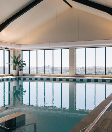 An indoor heated swimming pool within a barn style building with boho-chic styling and countryside views