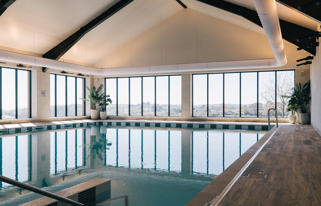 An indoor heated swimming pool within a barn style building with boho-chic styling and countryside views