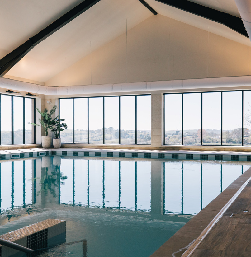 An indoor heated swimming pool within a barn style building with boho-chic styling and countryside views