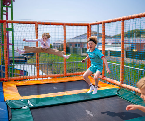 Three children jumping on elevated trampolines with views of the sea in the distance