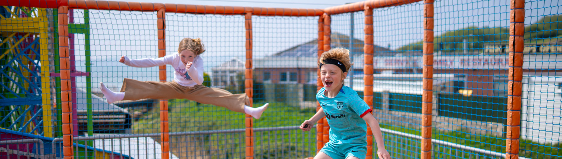 Three children jumping on elevated trampolines with views of the sea in the distance