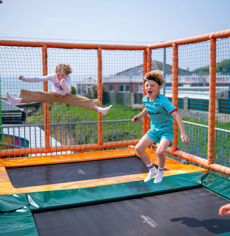Three children jumping on elevated trampolines with views of the sea in the distance